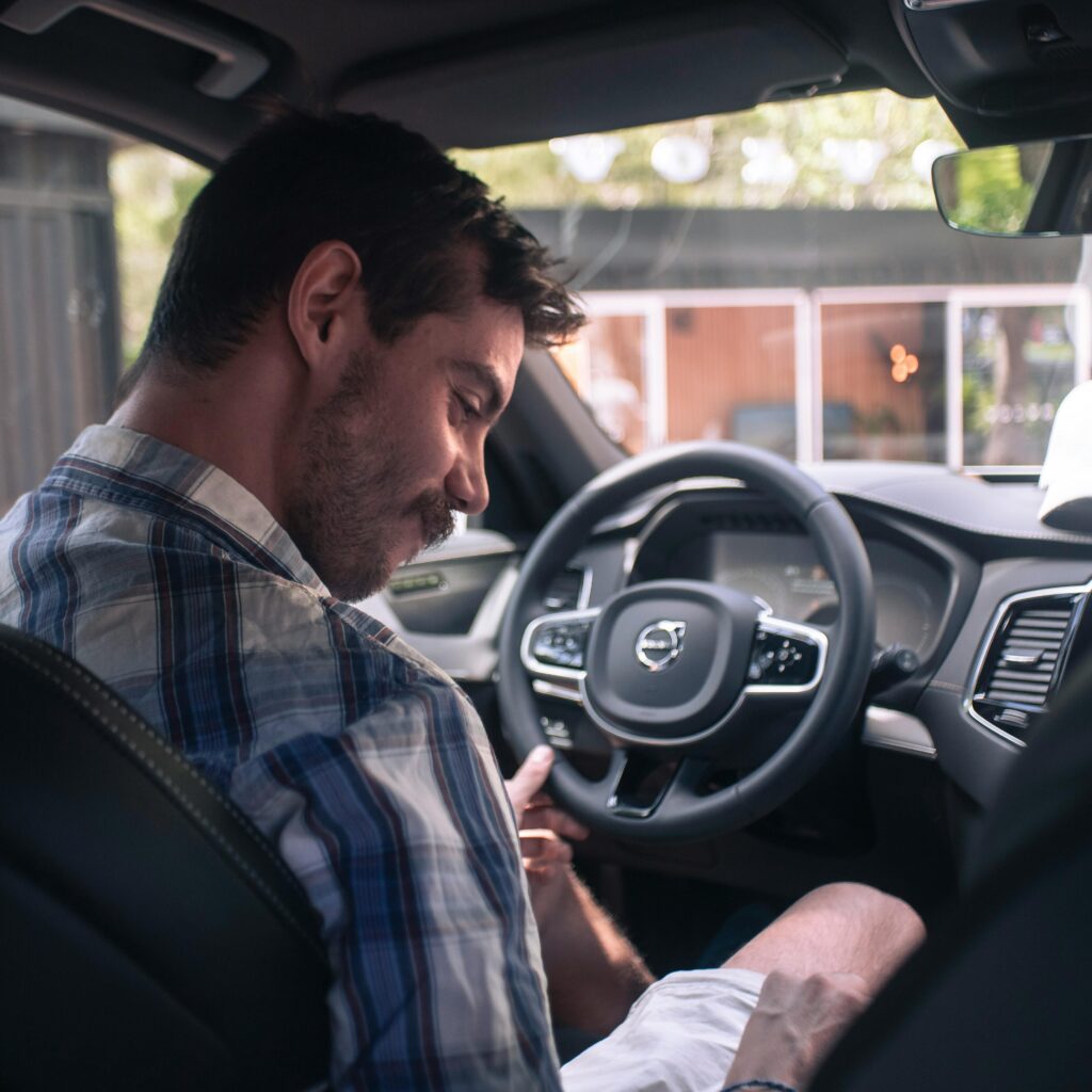 pexels-photo-15476320-15476320 Casually dressed man smiling in the driver seat of a modern Volvo XC90 car interior.