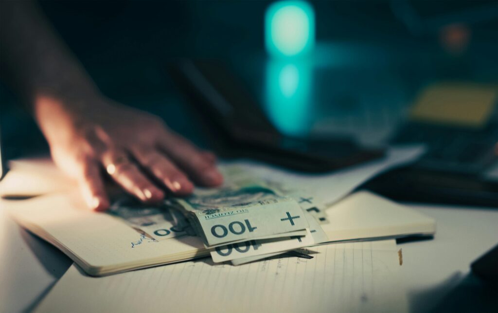 pexels-photo-35345780-35345780 Close-up of hand reaching for banknotes on an office desk with a notebook and calculator.