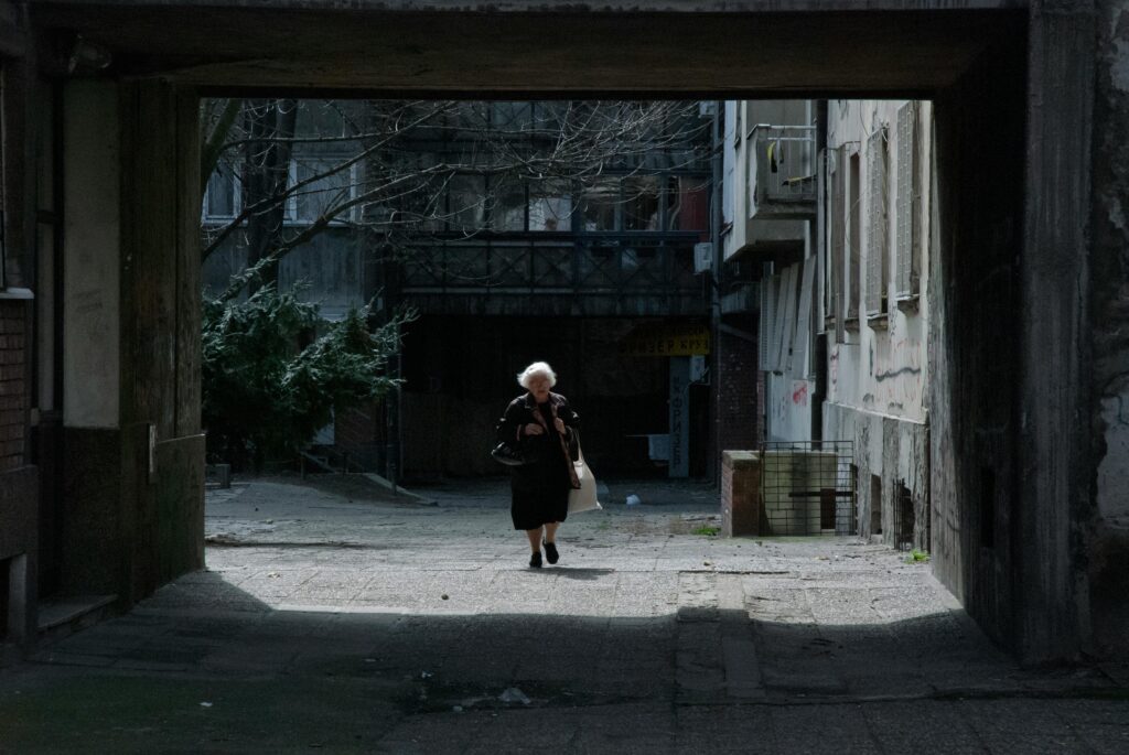 pexels-photo-28320578-28320578 A senior woman walks through a shadowy urban alley, highlighting solitude and resilience.