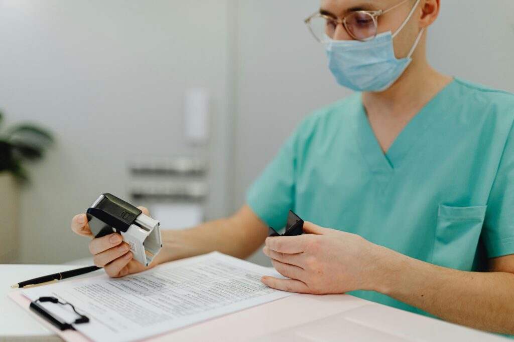 pexels-photo-6627938-6627938 Healthcare worker in scrubs reviewing patient files with a stamp and clipboard.