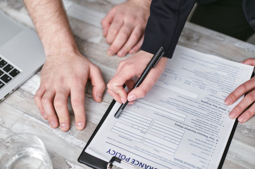 pexels-photo-7734574-7734574 Close-up image of two people signing an insurance policy document on a wooden desk.