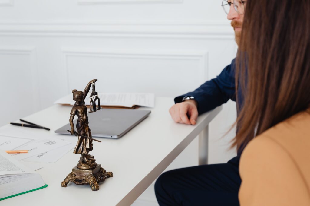 pexels-photo-7876314-7876314 Professional setting with lawyers and Lady Justice statue discussing legal documents.